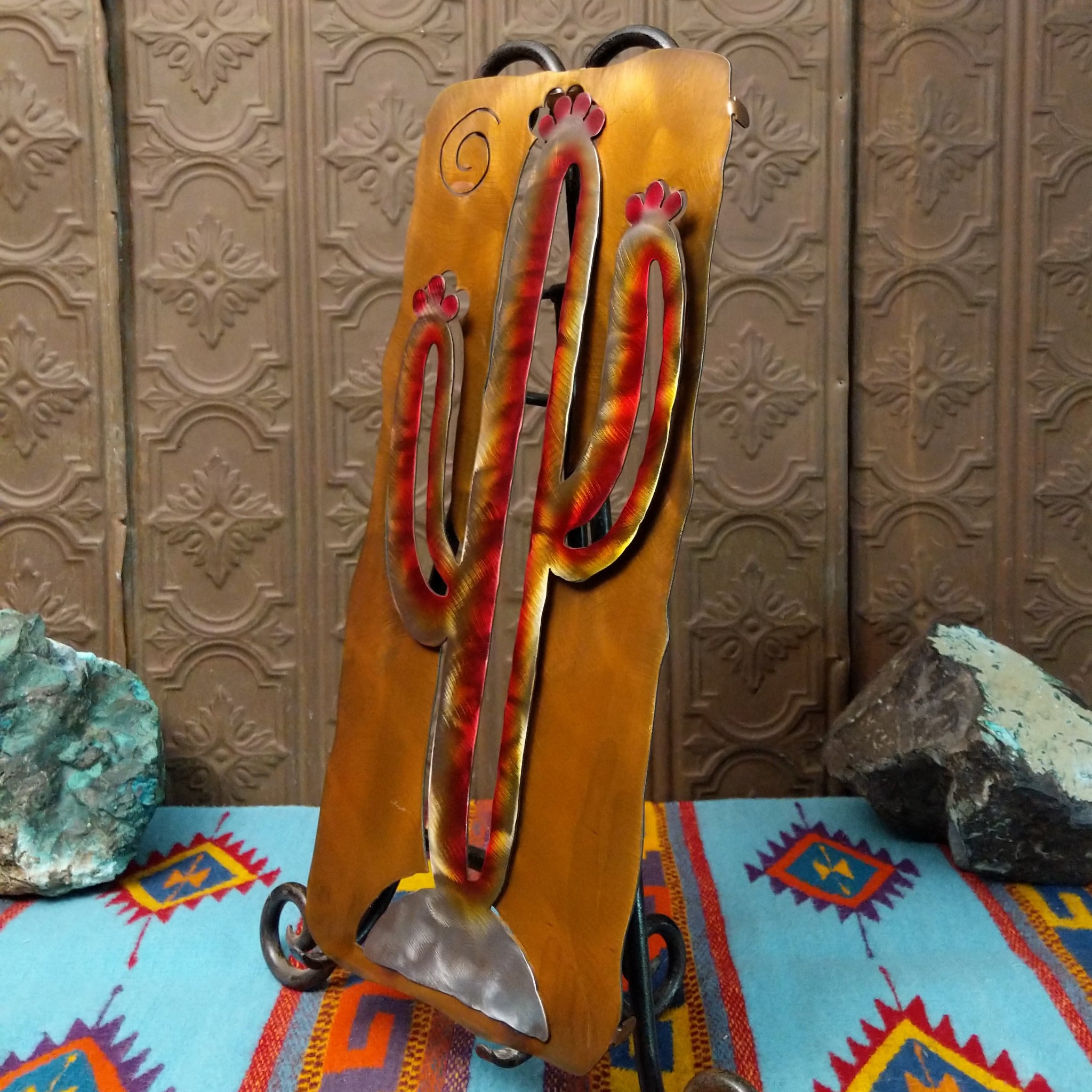 This 20-inch Crooks Design metal saguaro cactus features a red, yellow, and cream Sunset Swirl finish, silver-toned base, and warm golden-brown metal background; side view.