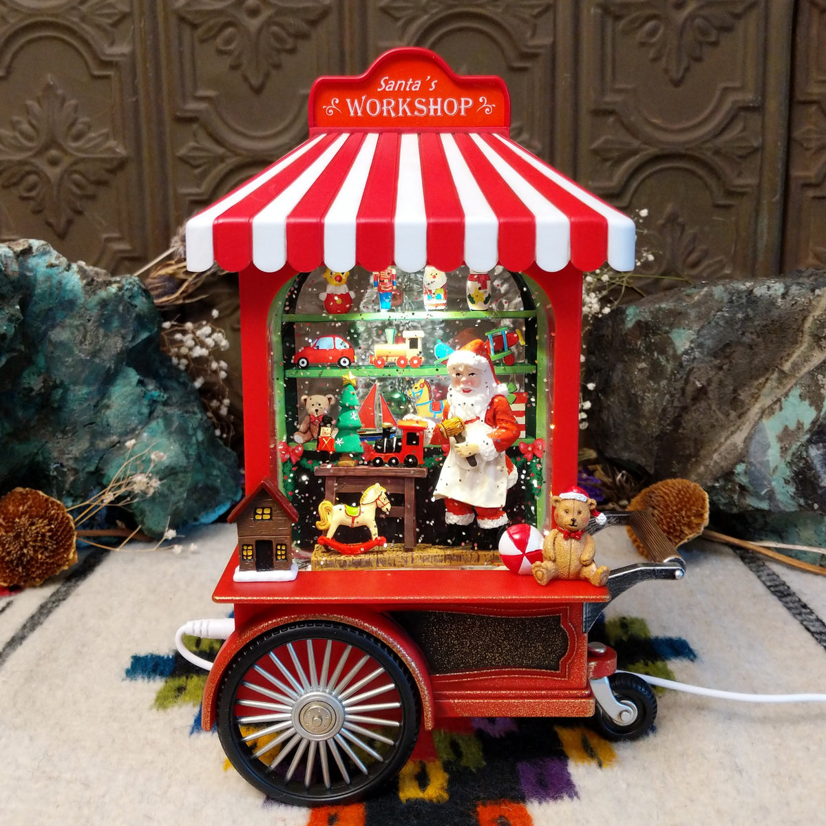 Santa’s Workshop Toy Cart Globe featuring Santa surrounded by miniature toys inside a red vintage-style cart with a red-and-white striped canopy and festive Christmas details.