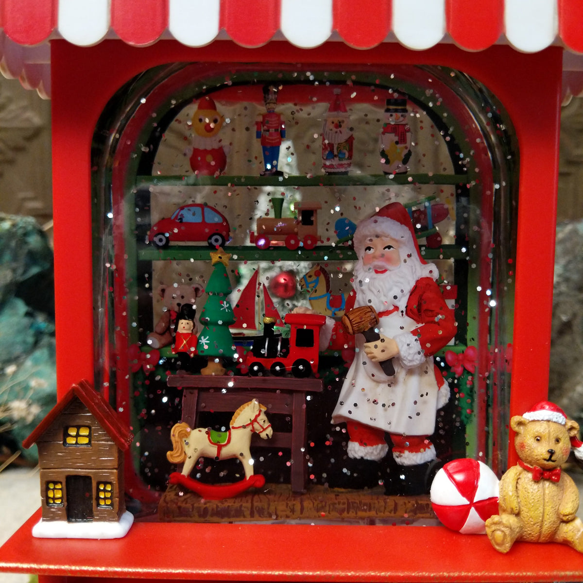 Santa’s Workshop Toy Cart Globe featuring Santa surrounded by miniature toys inside a red vintage-style cart with a red-and-white striped canopy and festive Christmas details.