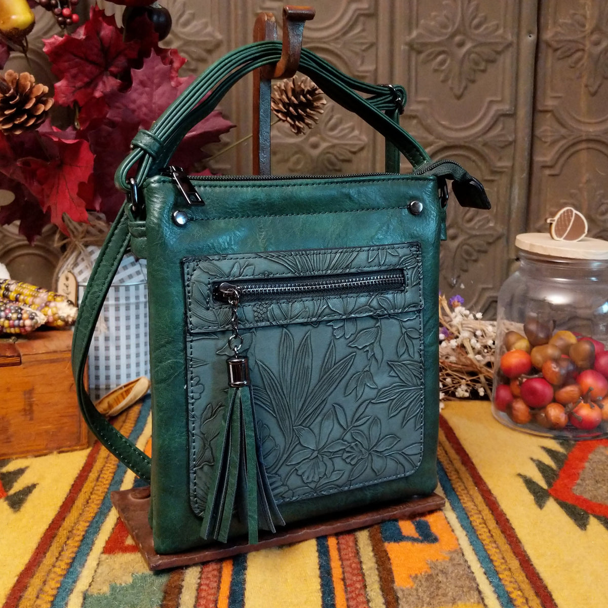 Sara Crossbody Bag by Liz Soto featuring a structured silhouette, embossed botanical front panel, zippered pocket, tassel zipper pull, top zip closure, and adjustable shoulder strap.