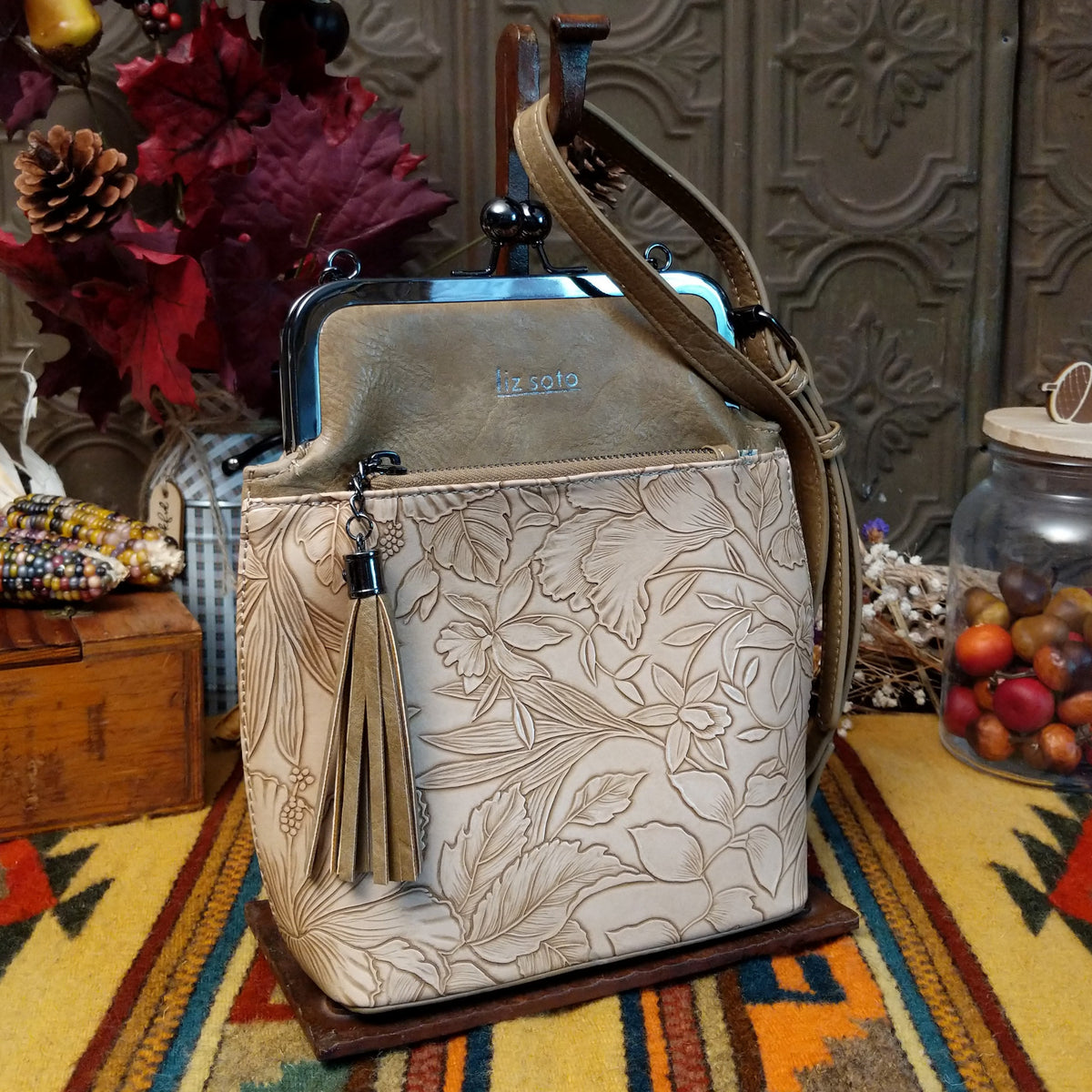 Selena Crossbody Bag by Liz Soto featuring embossed floral detailing, vintage-style kiss-lock frame closure, front zippered pocket, decorative tassel, and adjustable shoulder strap.