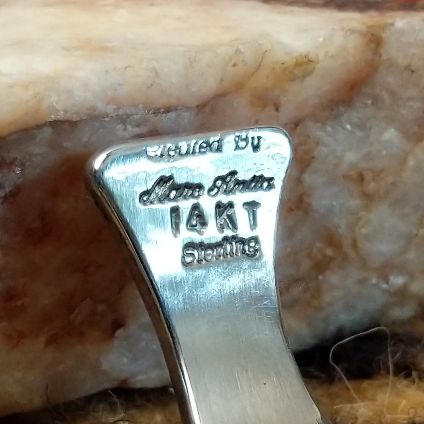 Close up of artist's stamped signature and stamped 14KT and Sterling, indicating 14 karat gold and sterling silver construction.