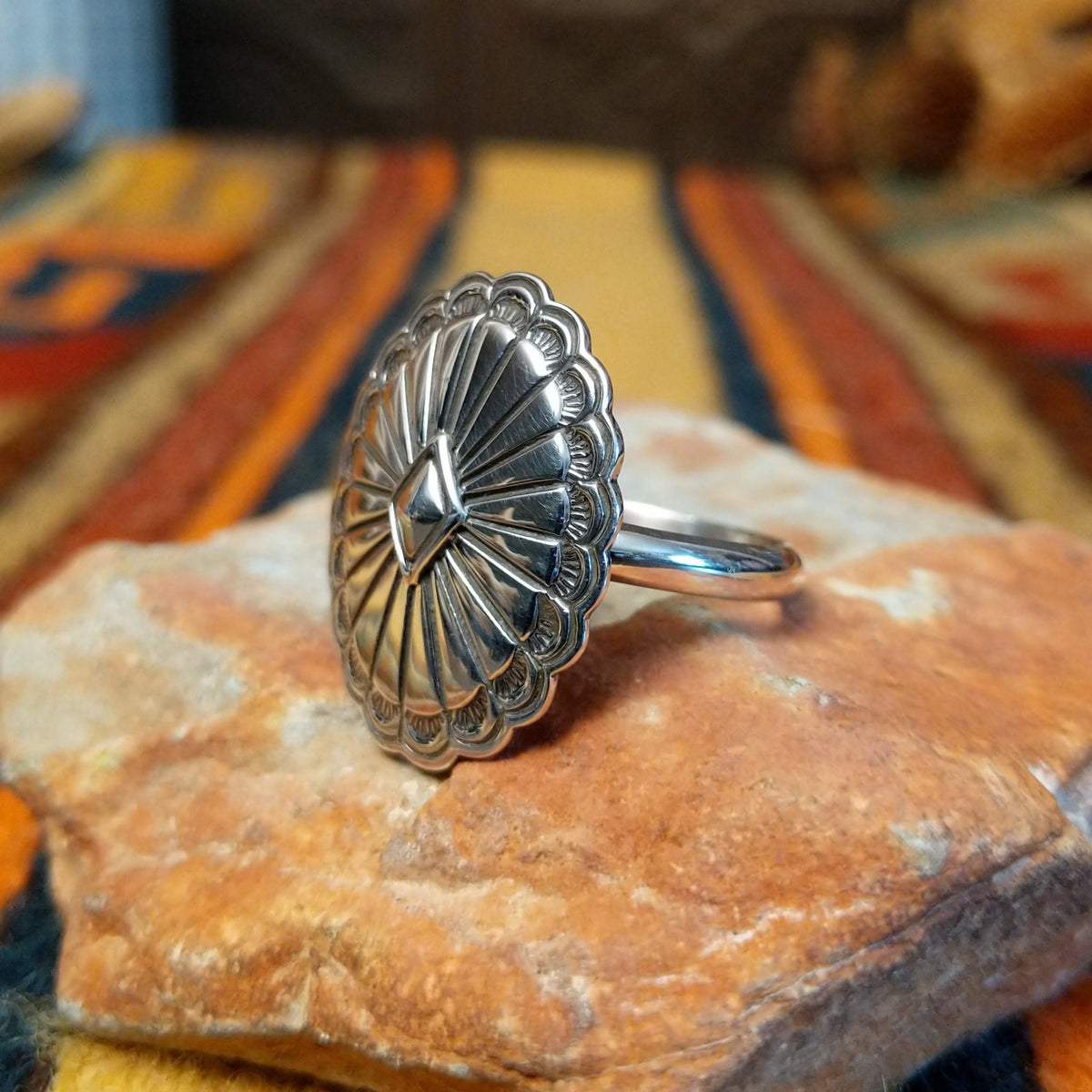 Silver Concho Ring by Elgin Tom featuring an oval silver concho with radiating stamped patterns, a raised diamond-shaped center, scalloped edges, and contrasting oxidized detailing; side view.