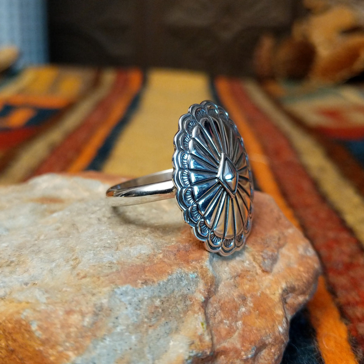Silver Concho Ring by Elgin Tom featuring an oval silver concho with radiating stamped patterns, a raised diamond-shaped center, scalloped edges, and contrasting oxidized detailing; side view.