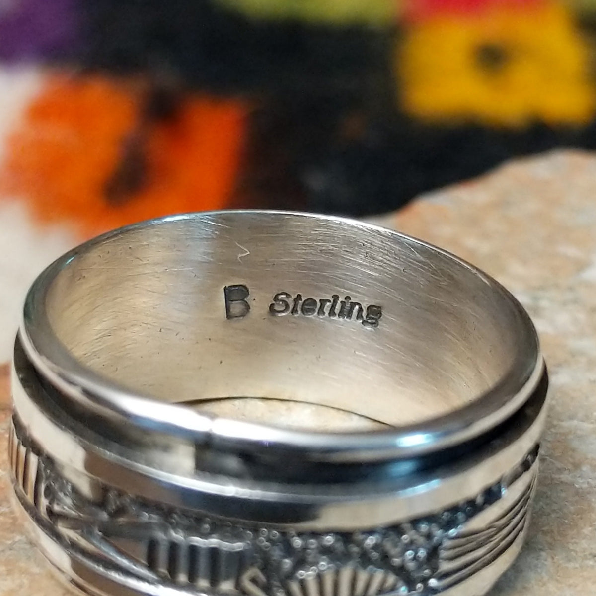 Silver spinner ring by Elaine Becenti with stamped geometric designs and layered movable bands. Close up of the artist's stamped signature.