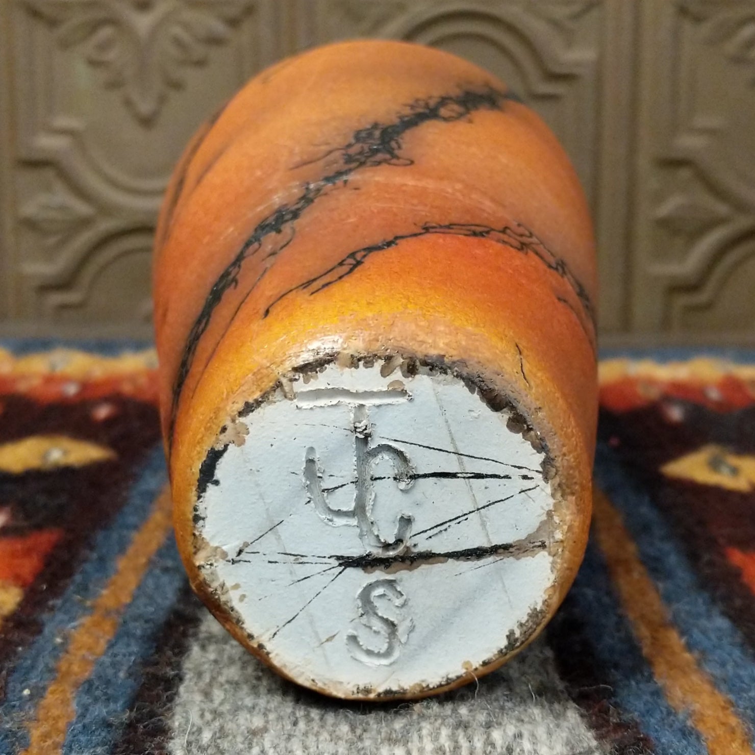 The base displays a rough terracotta texture with the artist’s signature.