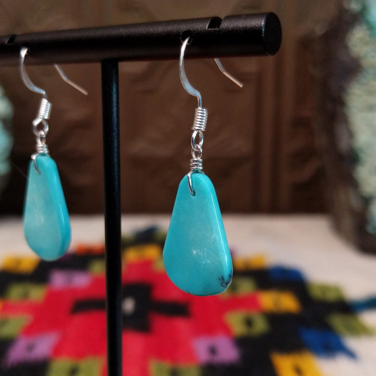 Smooth Navajo turquoise slab earrings featuring polished blue teardrop-shaped stones with minimal natural matrix, suspended from silver hooks; side view.