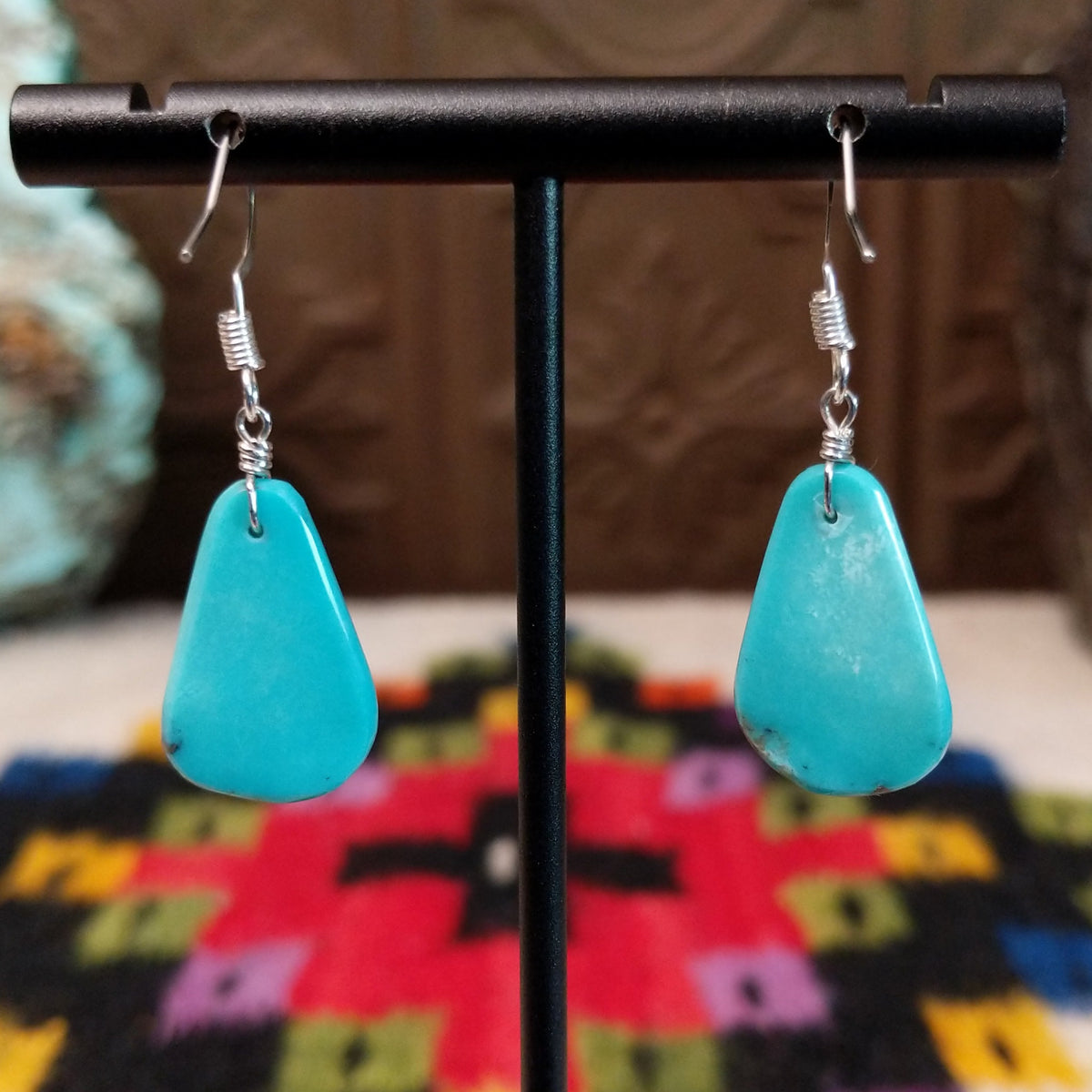 Smooth Navajo turquoise slab earrings featuring polished blue teardrop-shaped stones with minimal natural matrix, suspended from silver hooks; backside view.