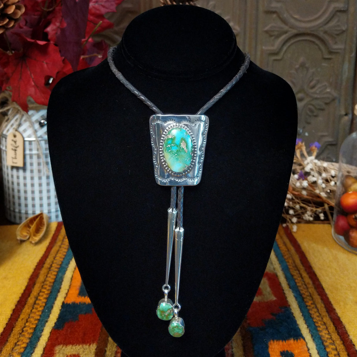 A Sterling Silver bolo-style necklace displayed on a black velvet mannequin bust. The necklace features a rectangular silver pendant with a large Sonoran Gold Turquoise stone, a black braided cord, and two dangling Sonoran Gold Turquoise stones.