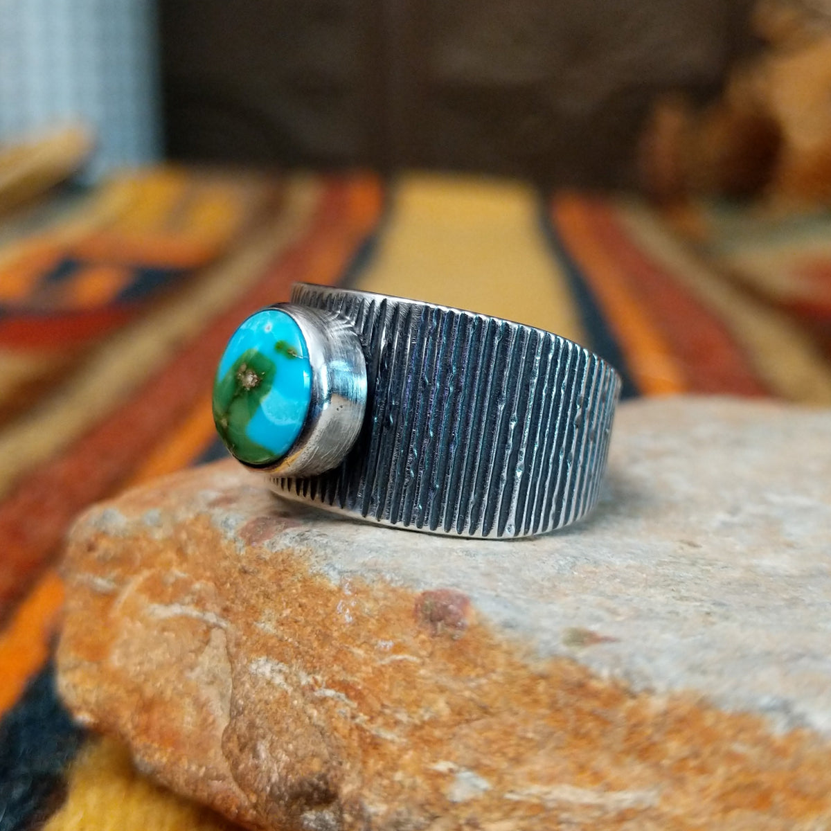 Sonoran Gold Turquoise Ring by Elgin Tom featuring a round blue and green turquoise stone with natural matrix, set in a wide sterling silver band with textured vertical lines; side view.