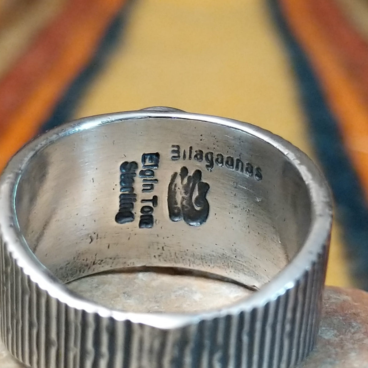 Sonoran Gold Turquoise Ring by Elgin Tom featuring a round blue and green turquoise stone with natural matrix, set in a wide sterling silver band with textured vertical lines; artisan and Sterling Silver stamp.