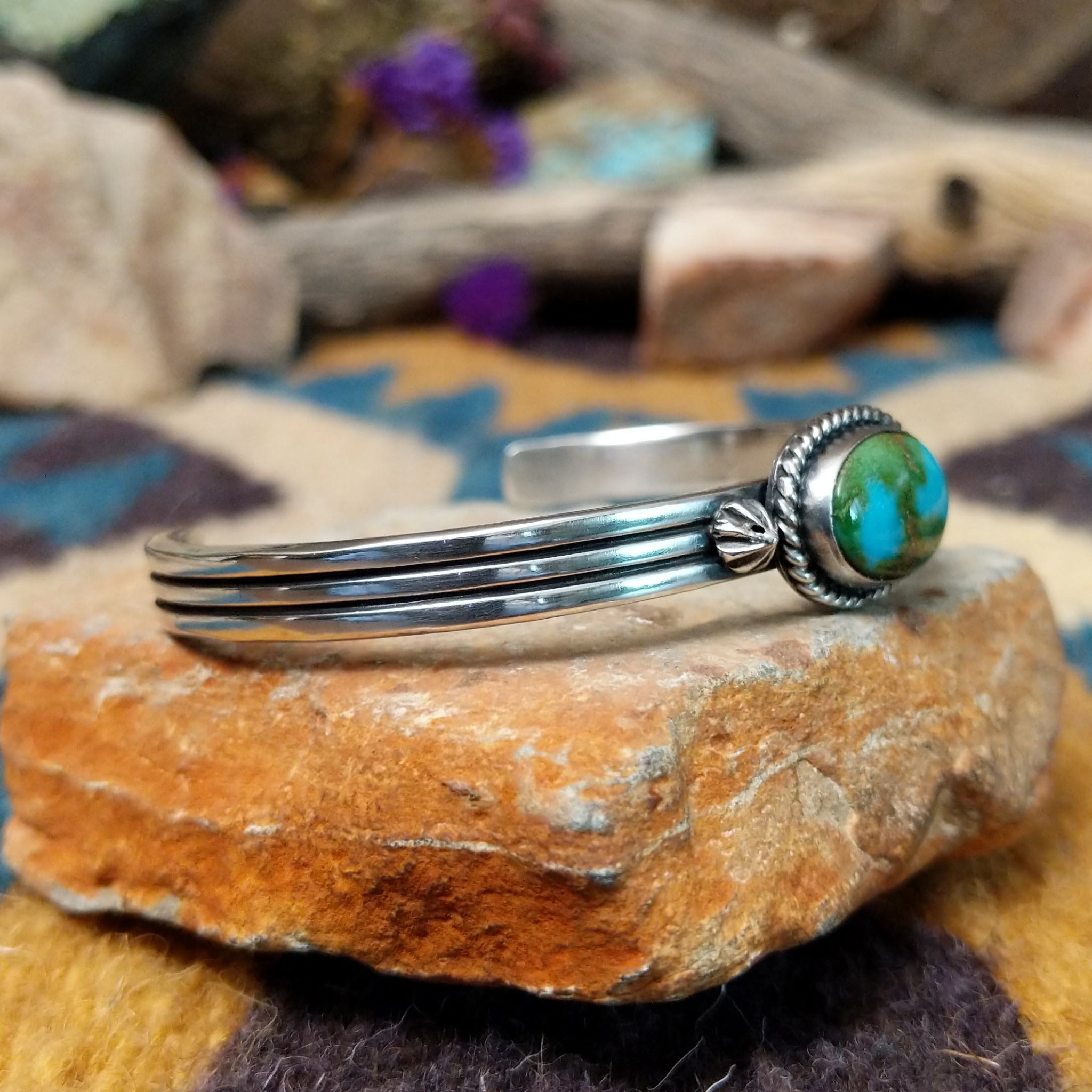 Handcrafted sterling silver cuff by Raymond Coriz featuring an oval Sonoran Gold turquoise cabochon in a twisted rope bezel on a three-wire cuff with hand-stamped fan accents; side view.