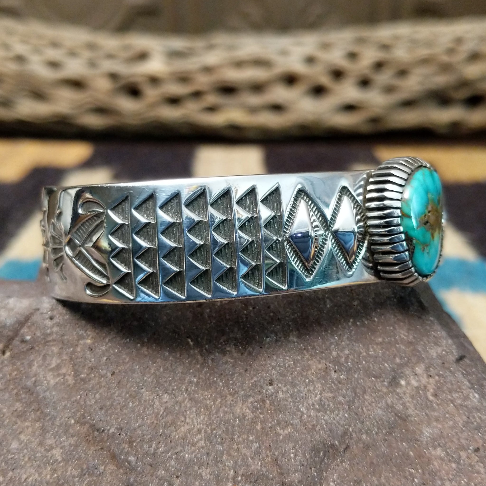 Sonoran Mountain turquoise cuff by Rydel Victor Curtis, featuring an oval blue Sonoran Mountain turquoise stone with natural golden-brown matrix set in a handcrafted sterling silver cuff with intricate geometric stampwork; side view.