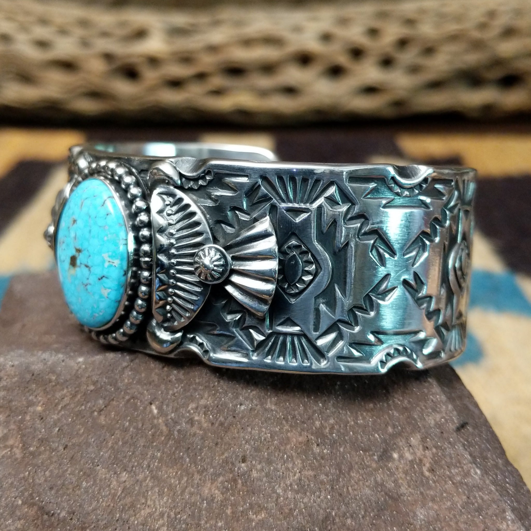 Spiderweb #8 turquoise cuff by Andrew Gordon, featuring an oval blue Spiderweb #8 turquoise stone with natural spiderweb matrix set in a handcrafted sterling silver cuff with hand-stamped fan and geometric designs; side view.