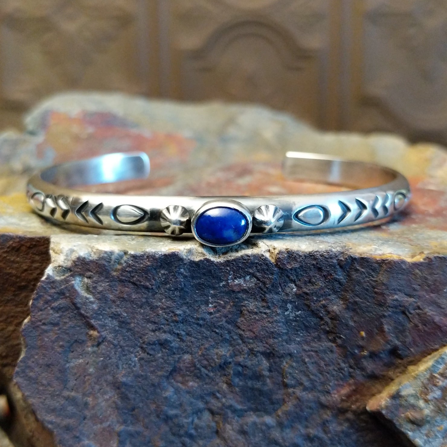 Sterling silver cuff bracelet with intricate stamping along the band and lapis set in the round bezel.