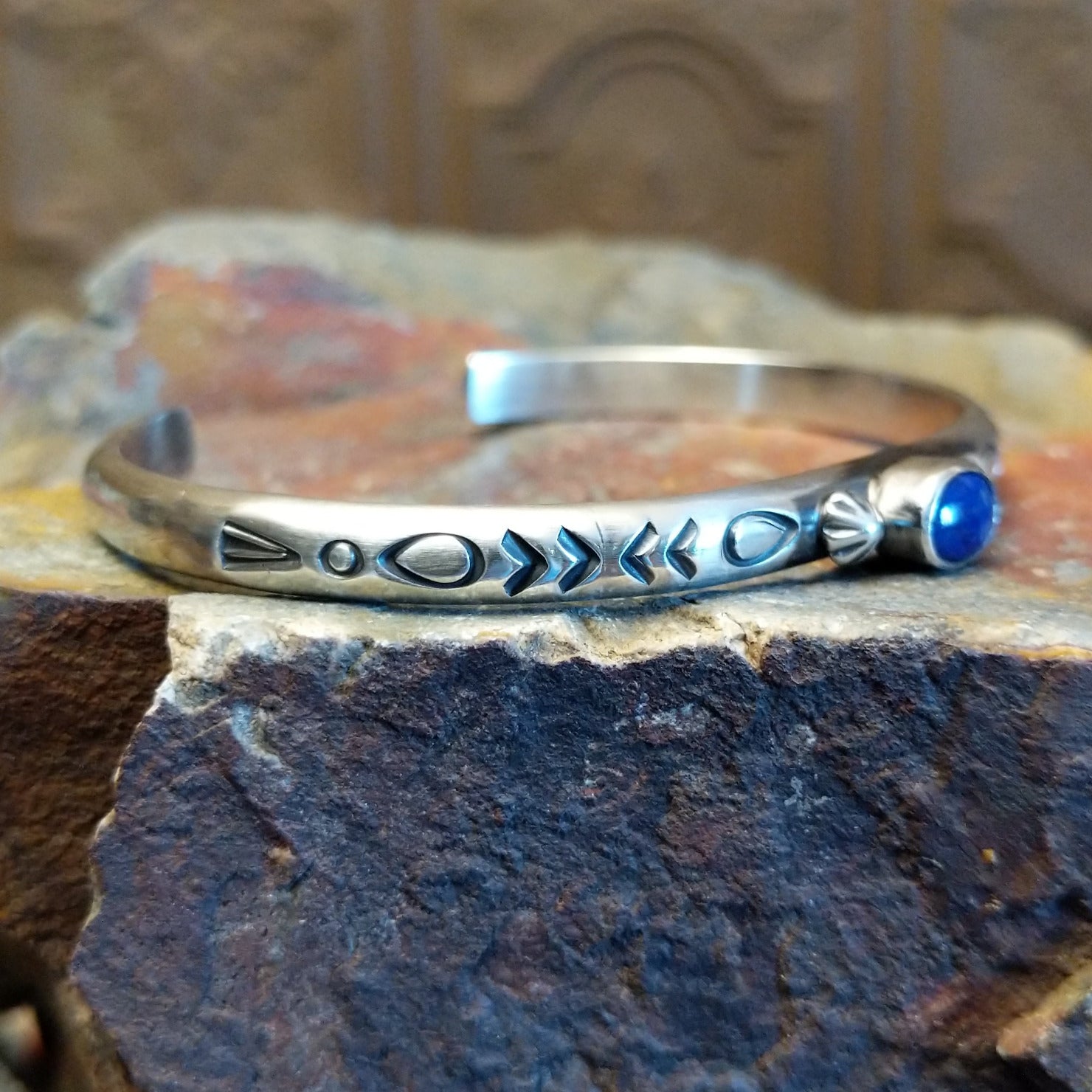 Sterling silver cuff bracelet with intricate stamping along the band and lapis set in the round bezel.