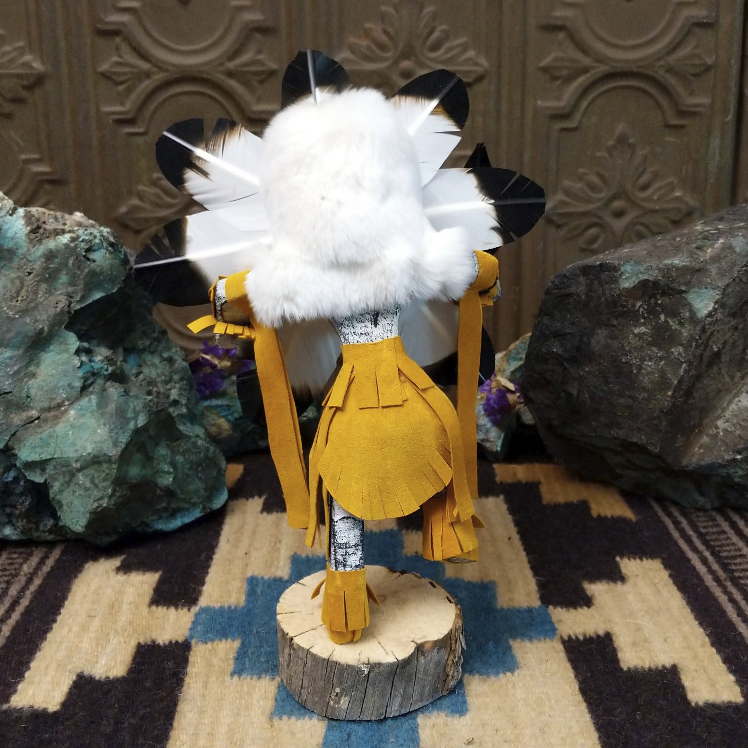 Navajo-made Sunface kachina doll by M. C. with circular multicolored mask, white feather halo, and yellow garments.