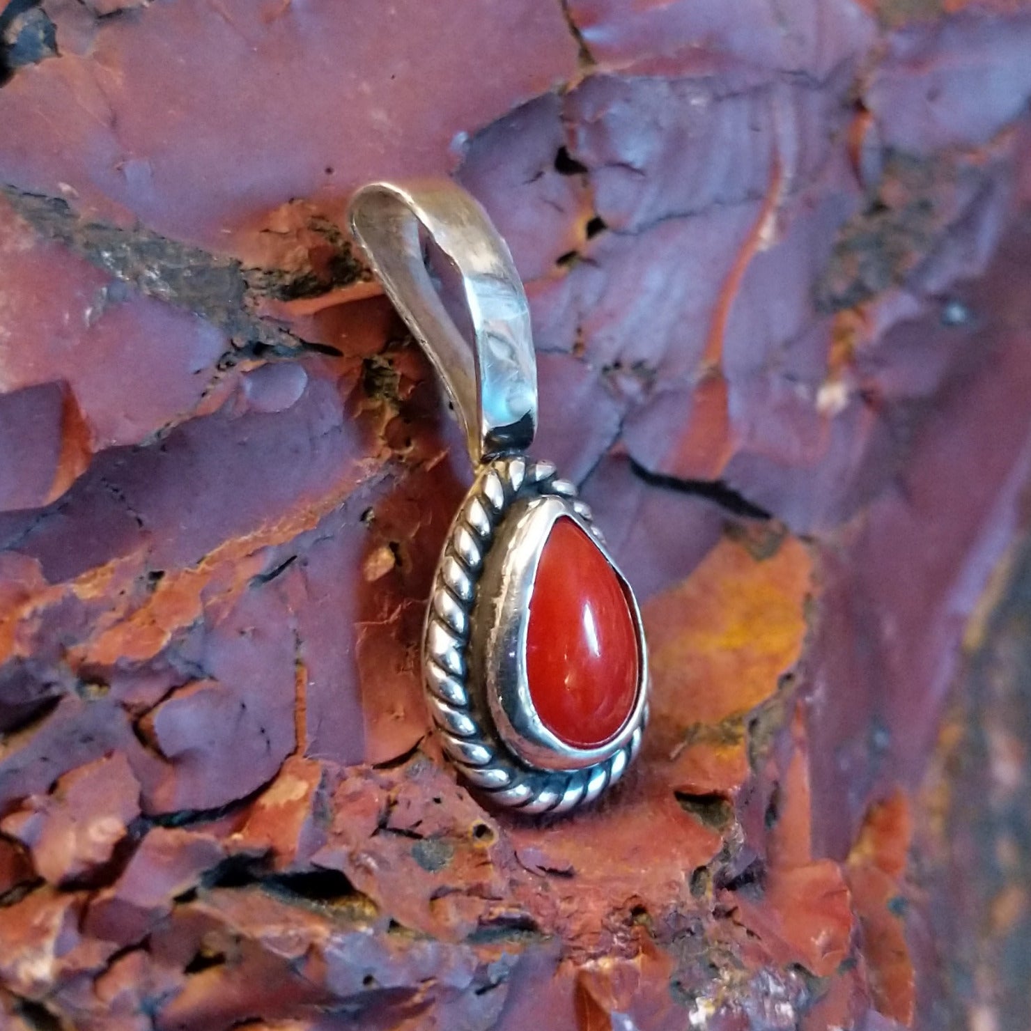 Teardrop-shaped pendant with coral, framed by twisted rope accent.