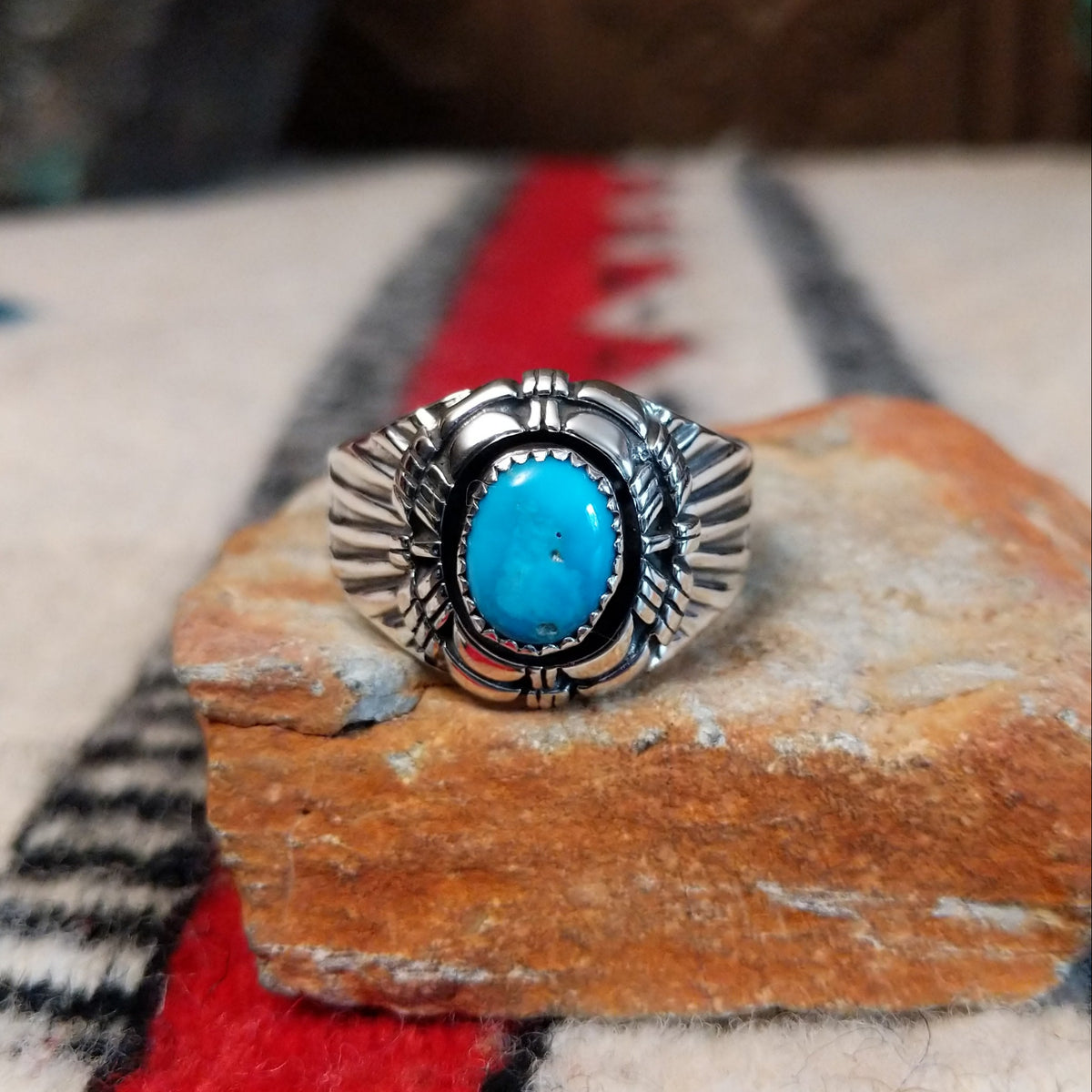 Turquoise ring by Roie Jaque featuring an oval bright blue turquoise stone in a serrated bezel, surrounded by layered, symmetrical silverwork with oxidized accents.