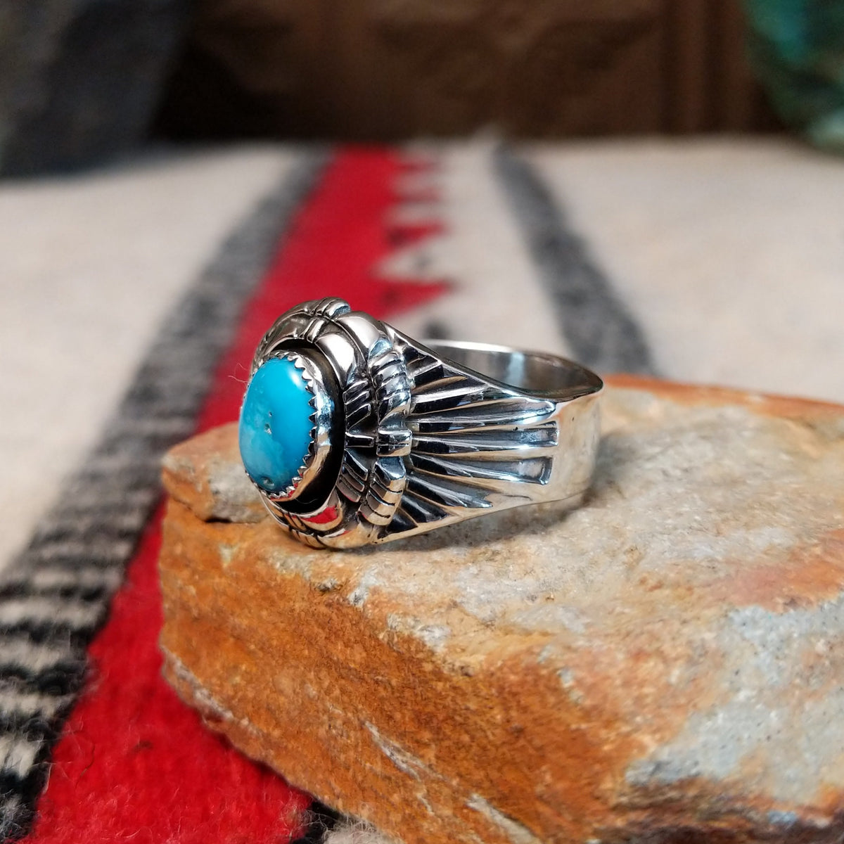 Turquoise ring by Roie Jaque featuring an oval bright blue turquoise stone in a serrated bezel, surrounded by layered, symmetrical silverwork with oxidized accents; side view.