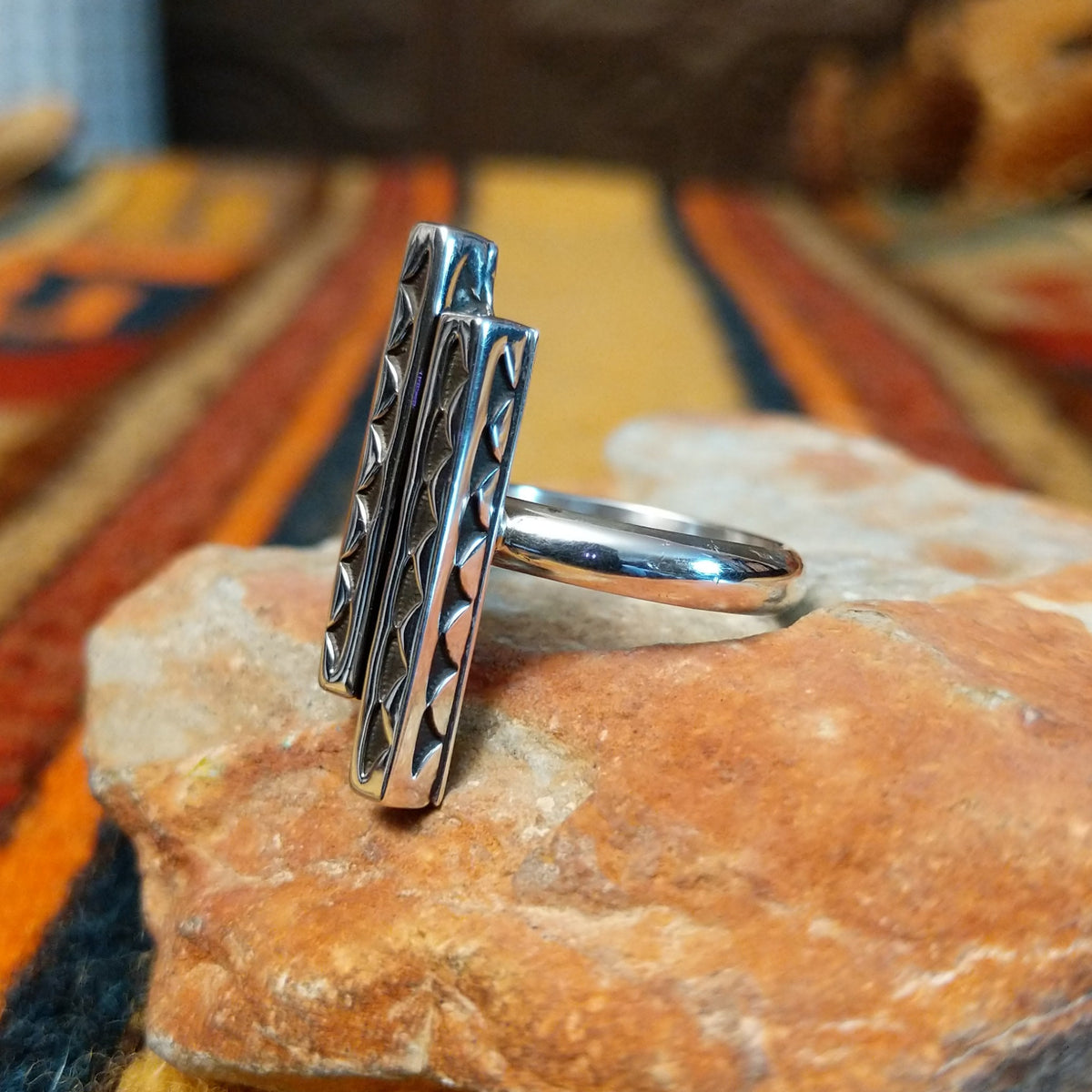 Angled view of a silver ring by Diane Wylie featuring two staggered vertical bars with recessed triangular stampwork and a smooth, rounded band.