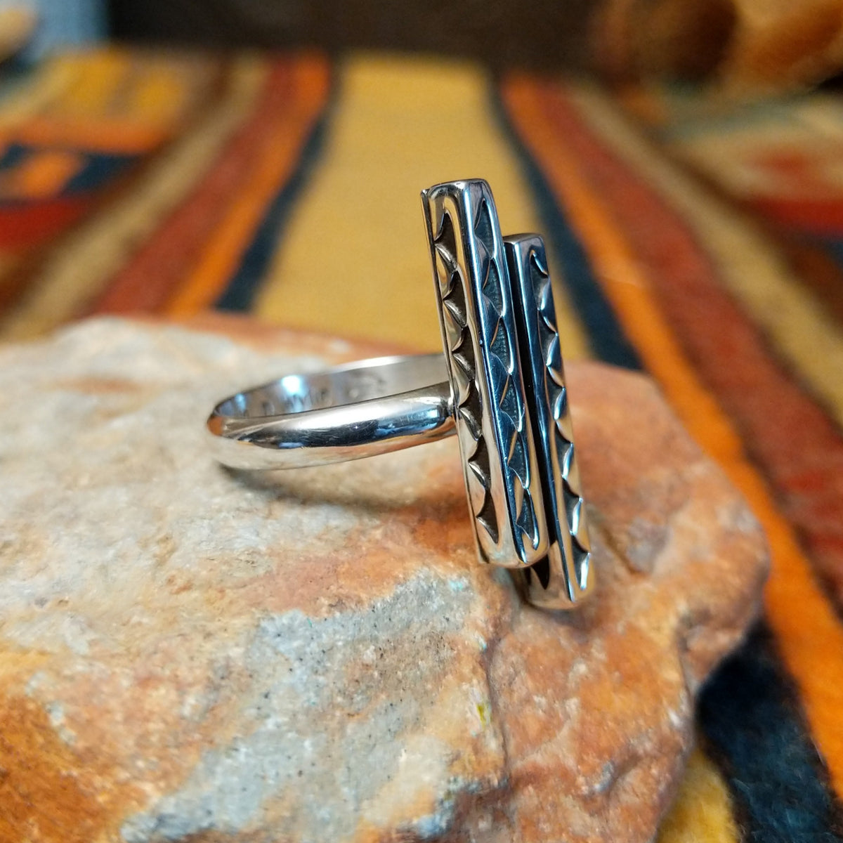 A silver ring by Diane Wylie featuring two staggered vertical bars with recessed triangular stampwork and a smooth, rounded band. Photo shows the ring from the opposite 3/4 view.