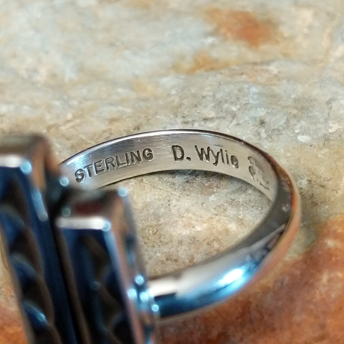Inside view of a silver ring by Diane Wylie showing two parallel bars of unequal height decorated with repeating triangular impressions and darkened detailing. Photo shows the artist's stamped signature.