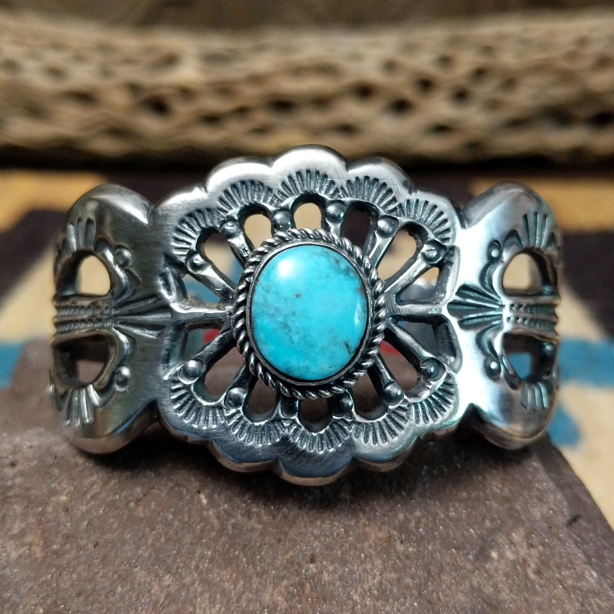 Turquoise cuff by Eugene Mitchell, featuring an oval blue turquoise stone set in a handcrafted sterling silver cuff with an intricate floral cutout design.