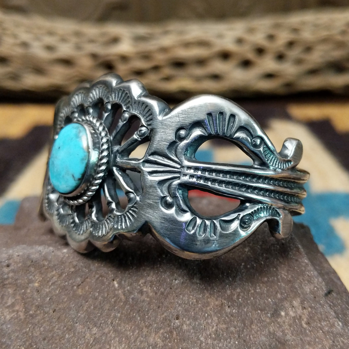 Turquoise cuff by Eugene Mitchell, featuring an oval blue turquoise stone set in a handcrafted sterling silver cuff with an intricate floral cutout design; side view.