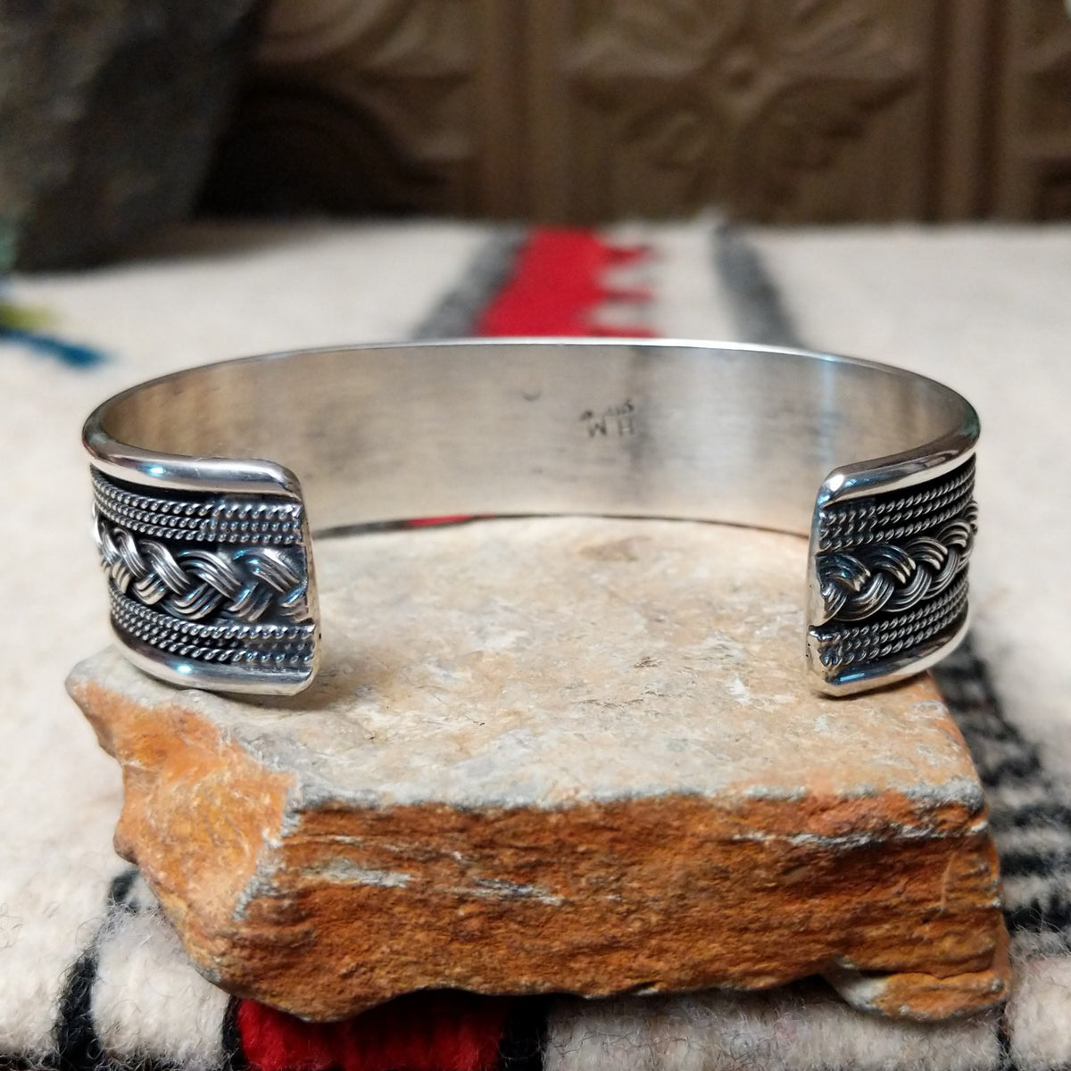 Silver cuff by H.M. featuring an oval blue turquoise stone with brown matrix, centered over an intricate braided silver band with twisted-wire detailing and oxidized accents; underside view.