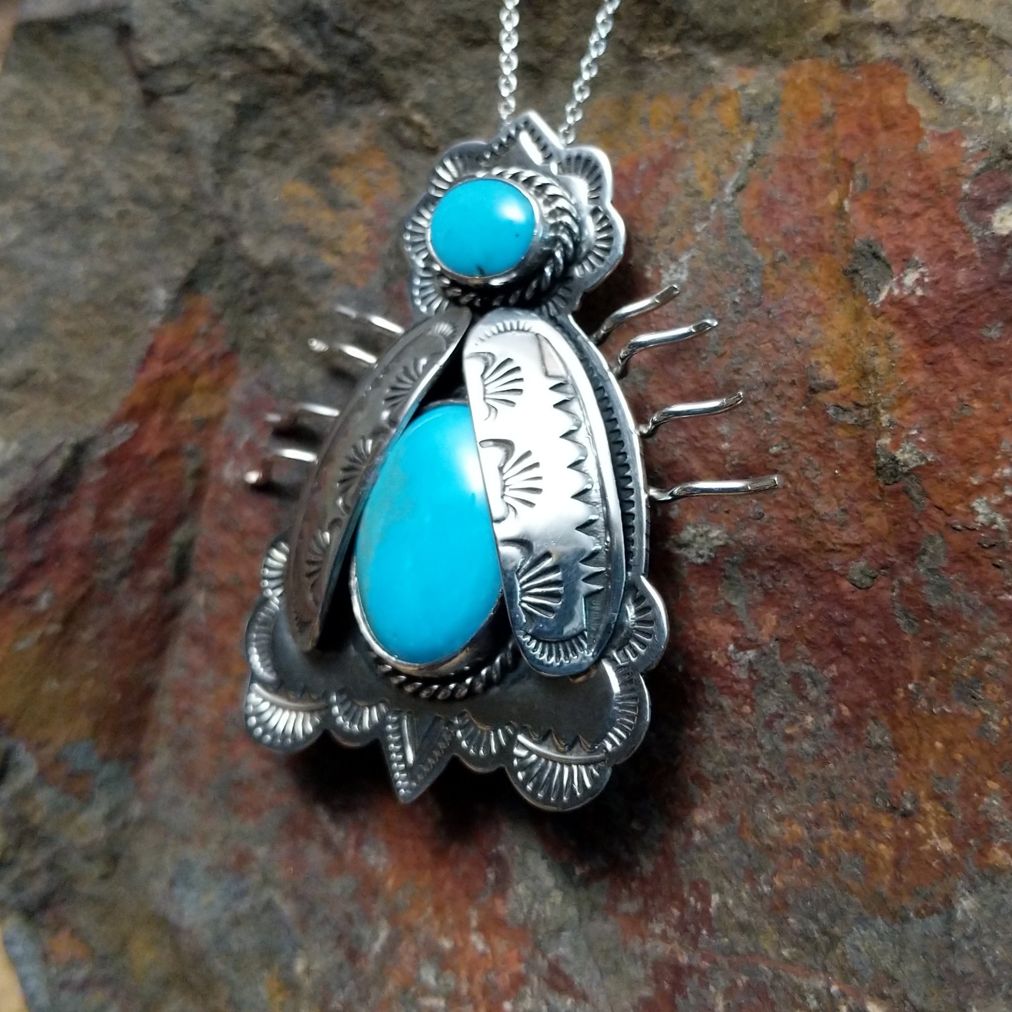 Handcrafted sterling silver bug pin with two turquoise stones and hand-stamped Navajo details; side view.