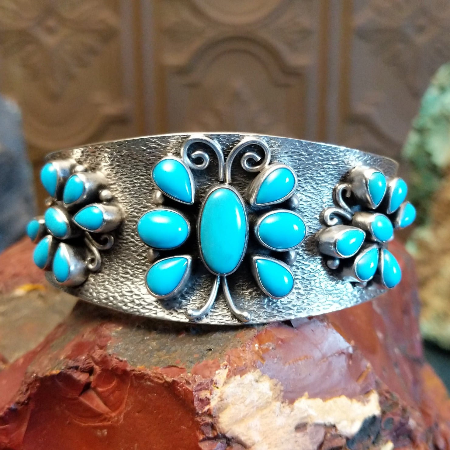 Sterling silver cuff bracelet features turquoise set in bezels creating butterfly motifs along the hammered surface.