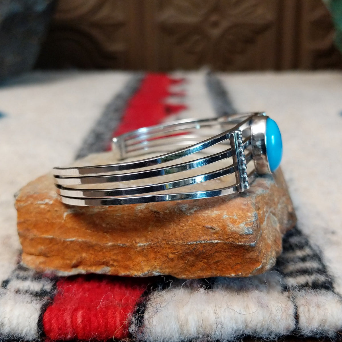 Silver cuff by Thomas Yazzie featuring a smooth oval blue turquoise stone centered within five slender silver bands and flanked by vertical beaded silver accents; side view.