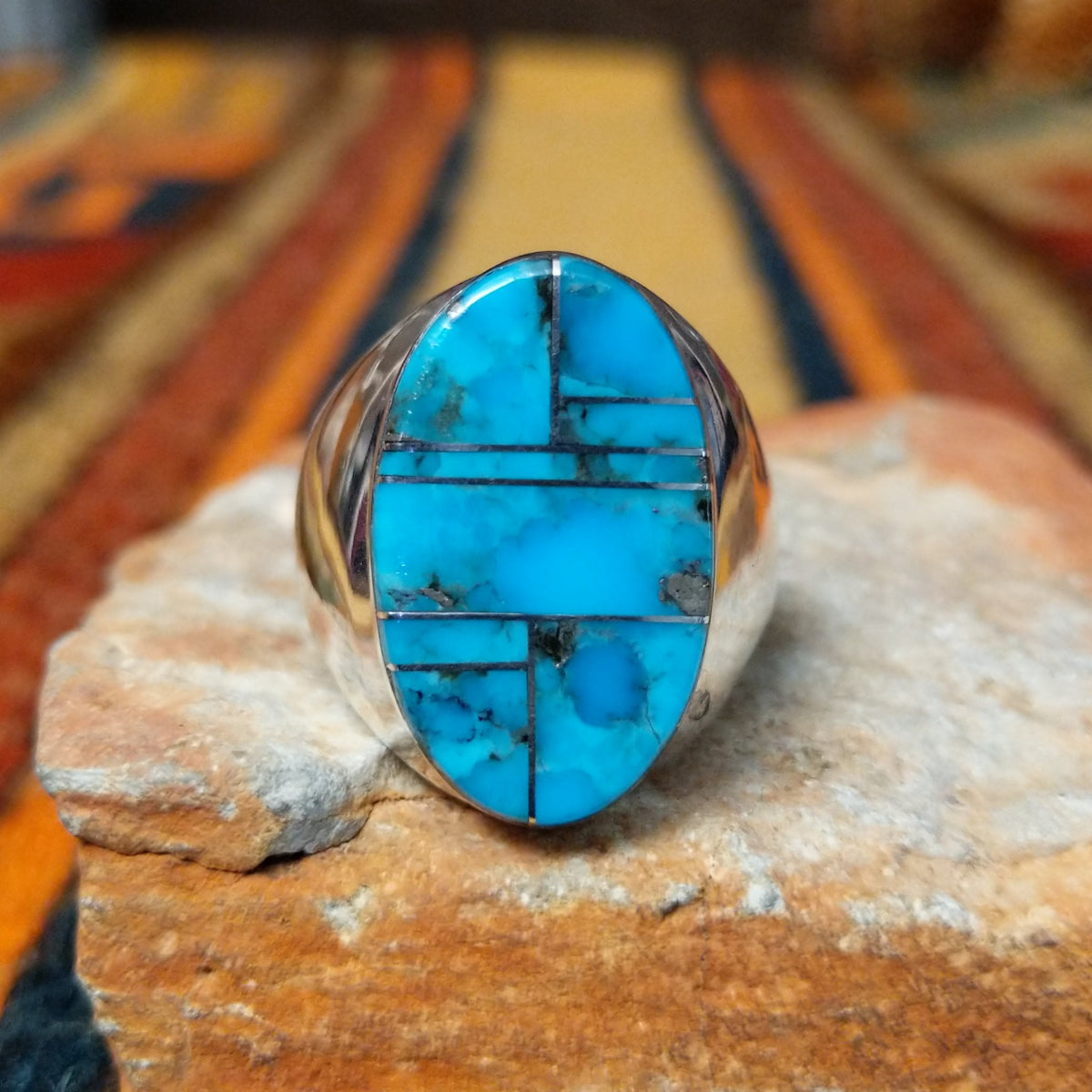 This striking Turquoise Inlay Ring by Wilbert Grey features a large oval face with vibrant blue turquoise, geometric silver inlay lines, natural dark matrix, and a polished silver band.