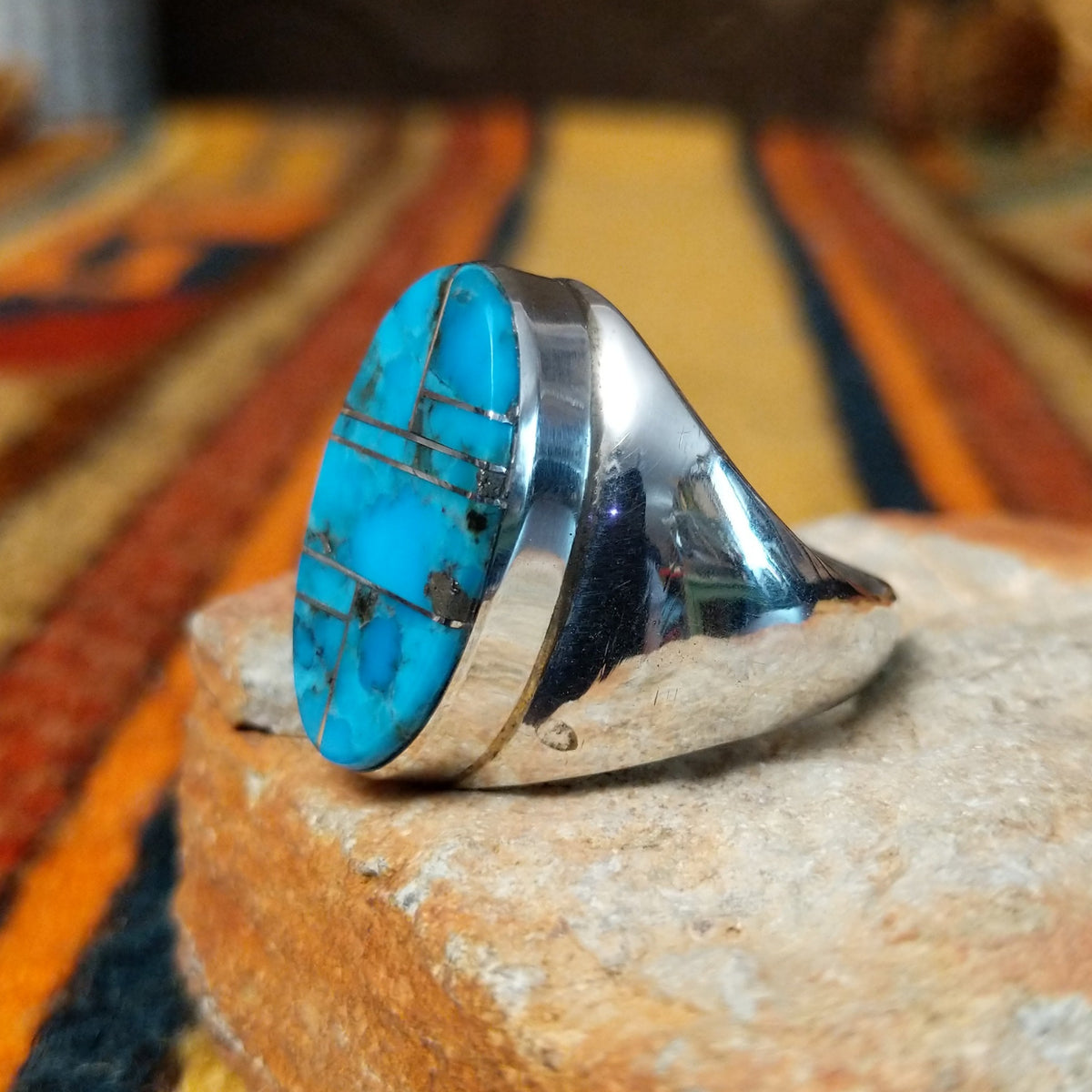 This striking Turquoise Inlay Ring by Wilbert Grey features a large oval face with vibrant blue turquoise, geometric silver inlay lines, natural dark matrix, and a polished silver band; side view.