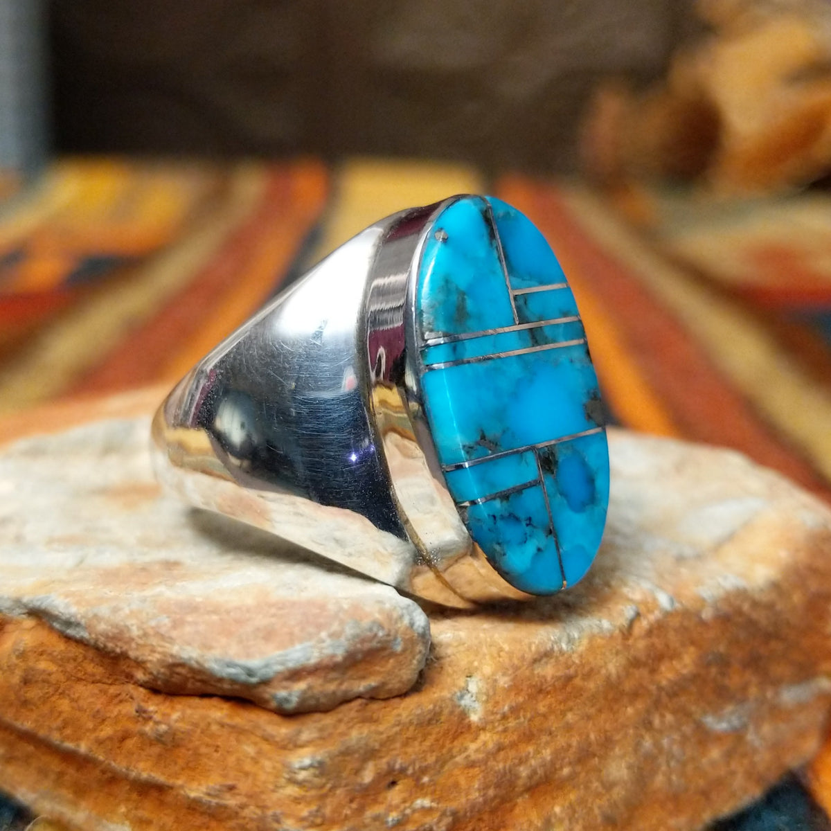 This striking Turquoise Inlay Ring by Wilbert Grey features a large oval face with vibrant blue turquoise, geometric silver inlay lines, natural dark matrix, and a polished silver band; side view.