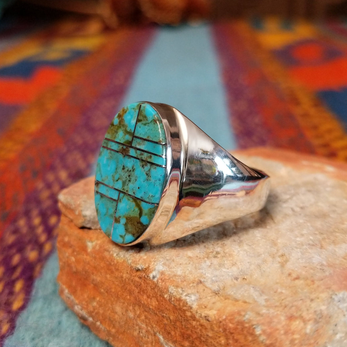Turquoise Inlay Ring by Wilbert Grey featuring an oval turquoise face with natural brown and green matrix, divided by geometric silver channels and set in a wide polished silver band; side view.