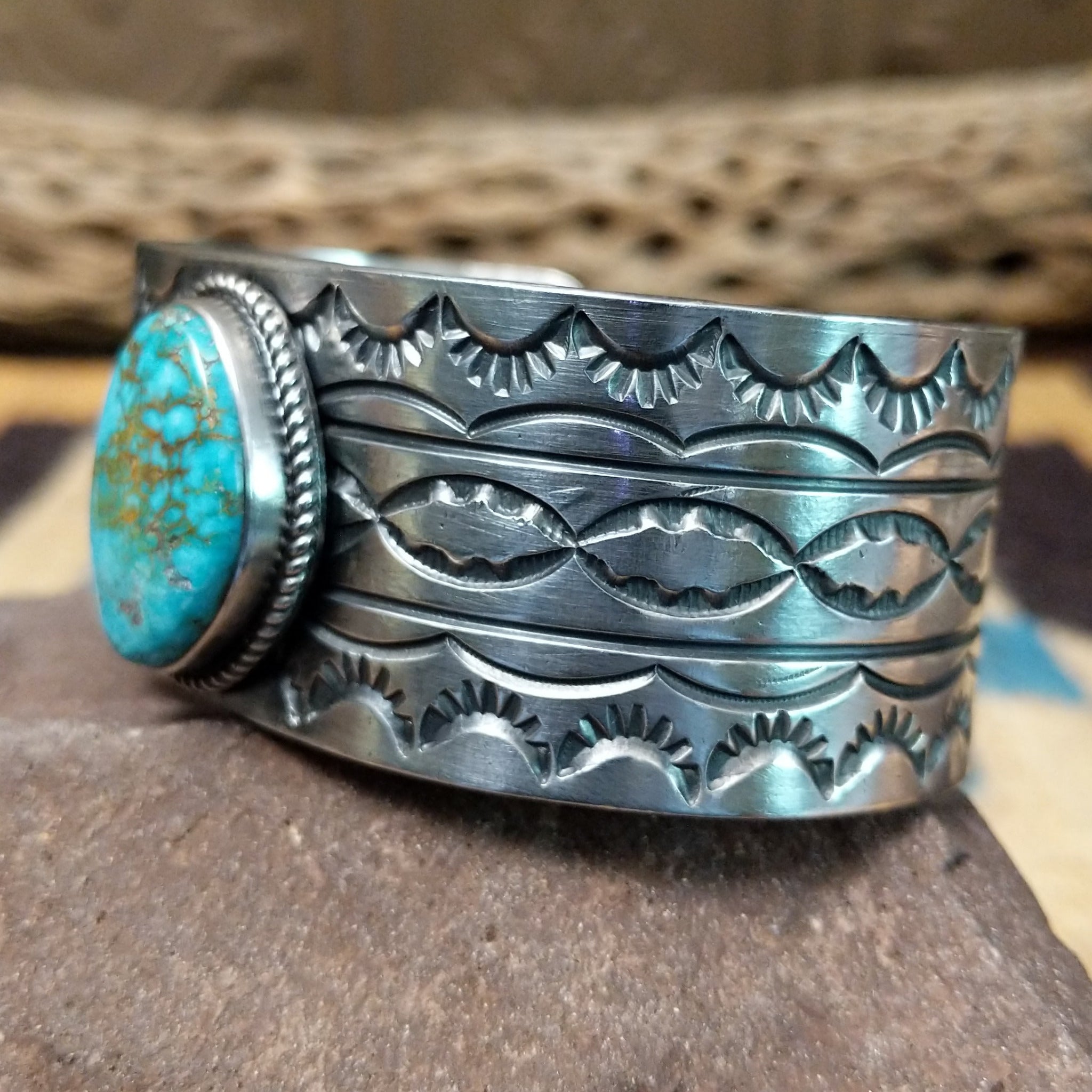 Turquoise Mountain turquoise cuff by E. Piaso, featuring a blue turquoise stone with a natural brown matrix set in a handcrafted wide sterling silver cuff; side view.