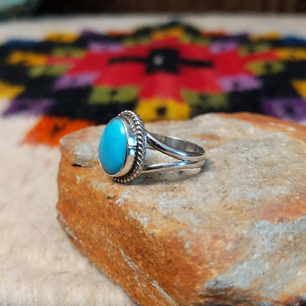 This Turquoise Ring by Byron Begay features a bright blue oval turquoise stone set in sterling silver with a twisted rope border and split-shank band; side view.
