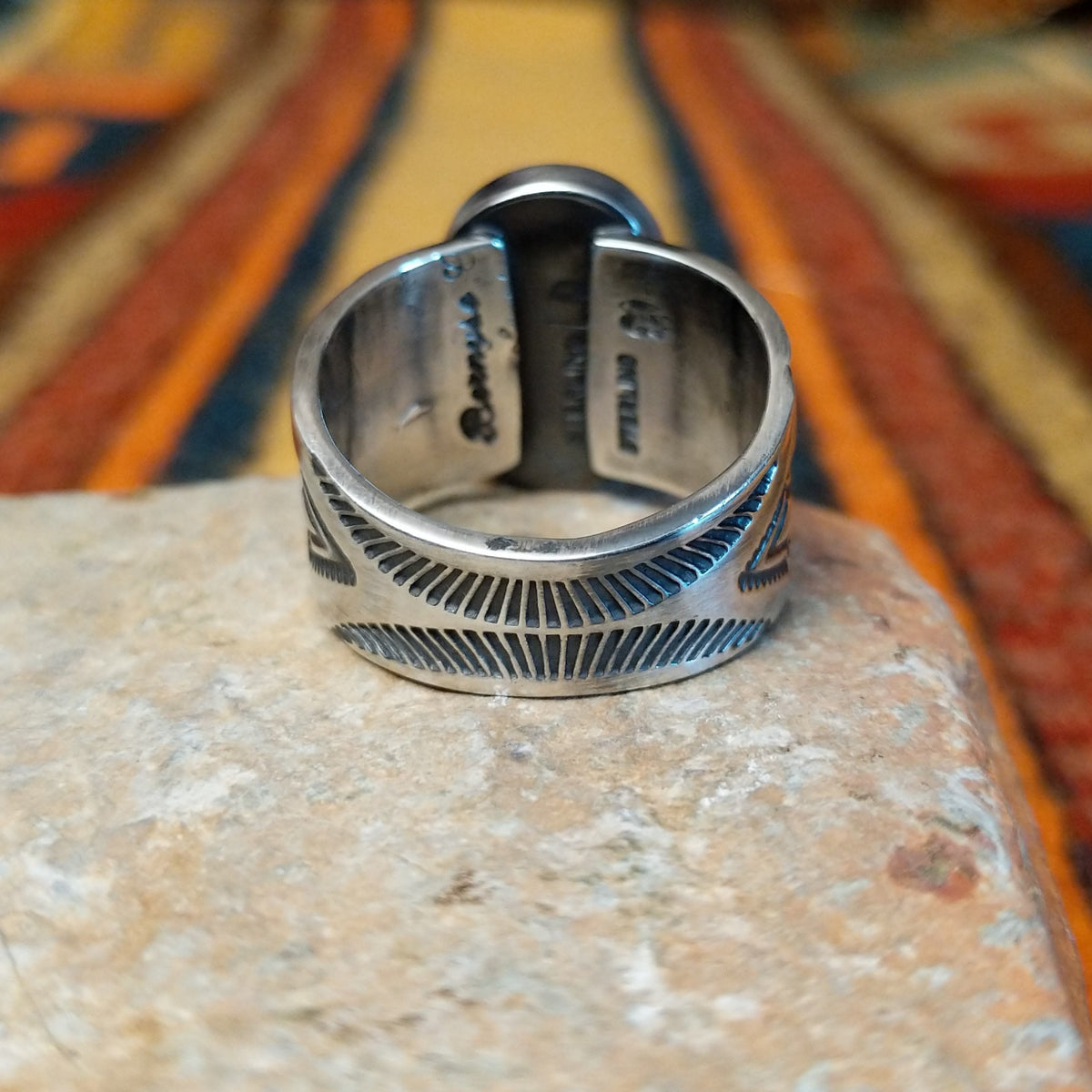 Turquoise Ring by Lowell Draper & Bernyse Chavez featuring a large oval turquoise stone with natural matrix, a polished silver bezel, and a wide silver band decorated with stamped sunburst patterns and geometric detailing; underside view.
