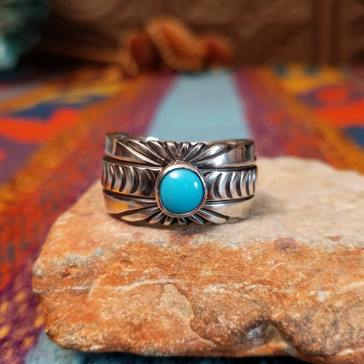 Turquoise Ring by Raymond Coriz featuring a round bright-blue turquoise cabochon centered on a wide silver band with hand-stamped curved and sunburst designs.