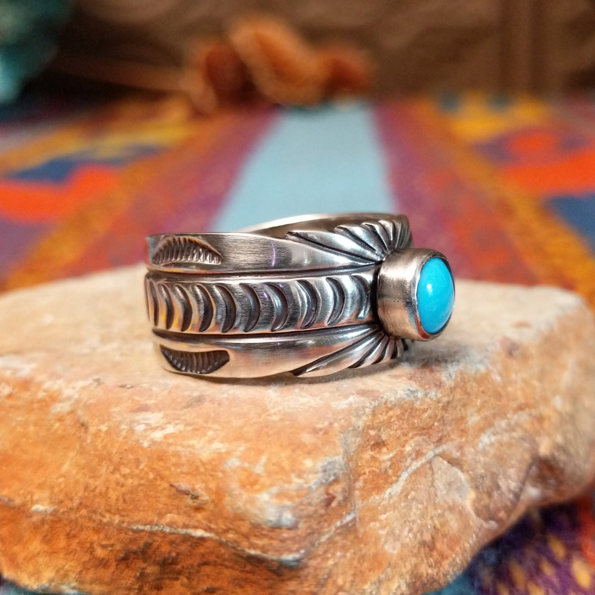 Turquoise Ring by Raymond Coriz featuring a round bright-blue turquoise cabochon centered on a wide silver band with hand-stamped curved and sunburst designs; side view.
