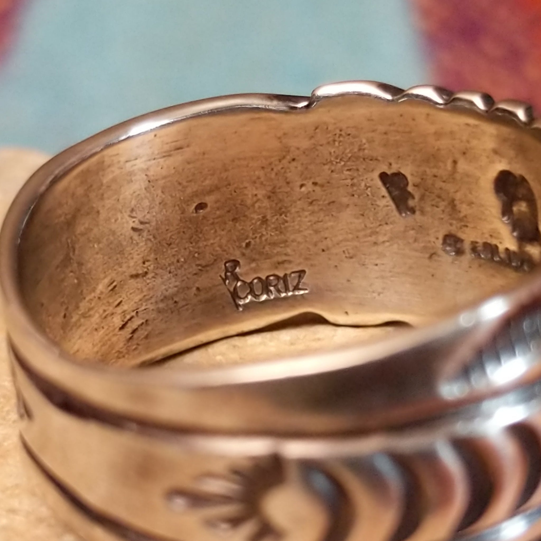 Turquoise Ring by Raymond Coriz featuring a round bright-blue turquoise cabochon centered on a wide silver band with hand-stamped curved and sunburst designs; artisan and Sterling Silver stamp.