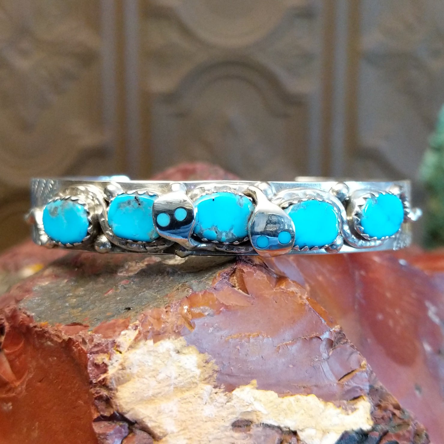 Sterling silver cuff bracelet with turquoise set in notched bezels and silverwork formed as a snake along the surface.