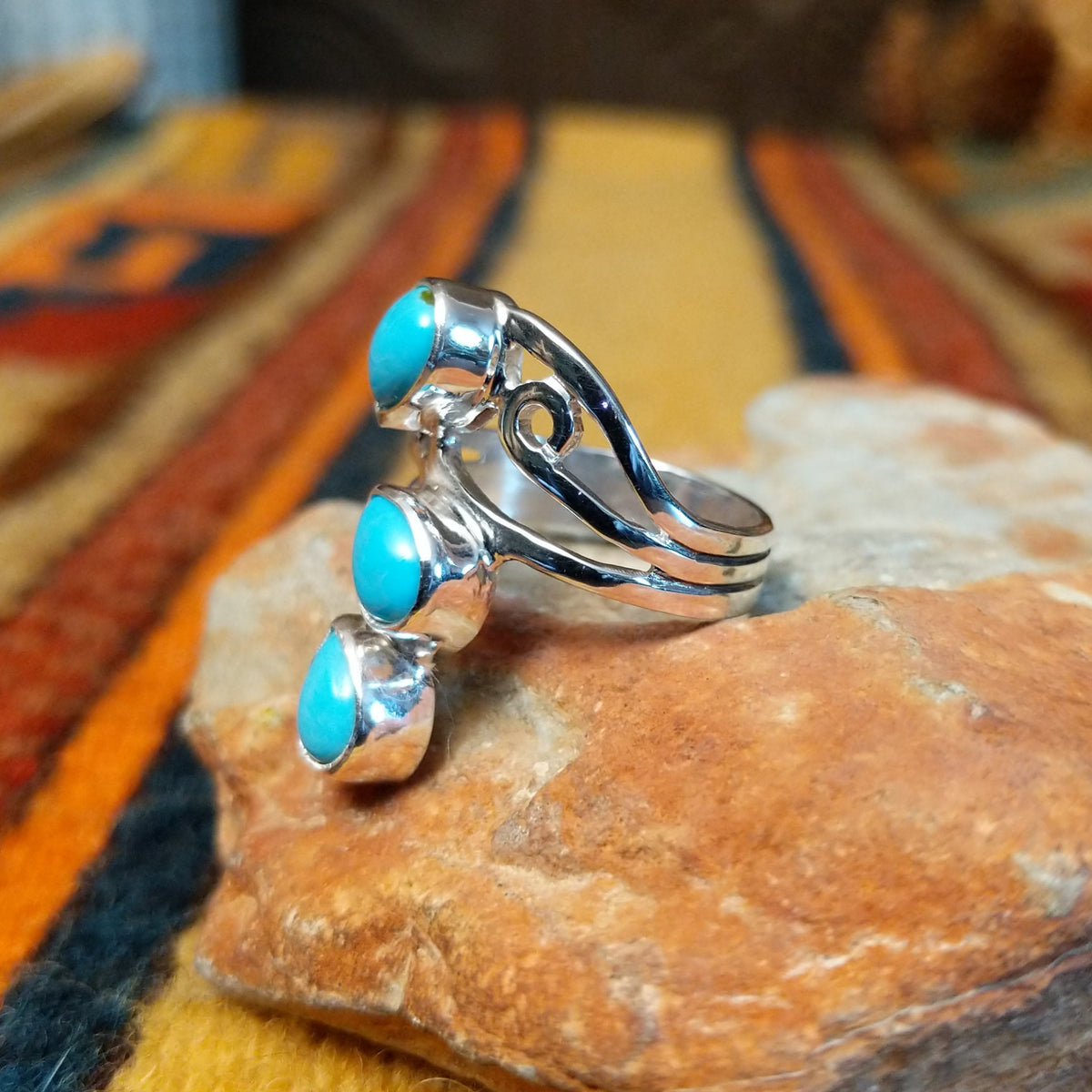 Side view of a turquoise ring showing three raised teardrop-shaped stones, an open silver setting, and a split-shank band with a curled spiral detail.