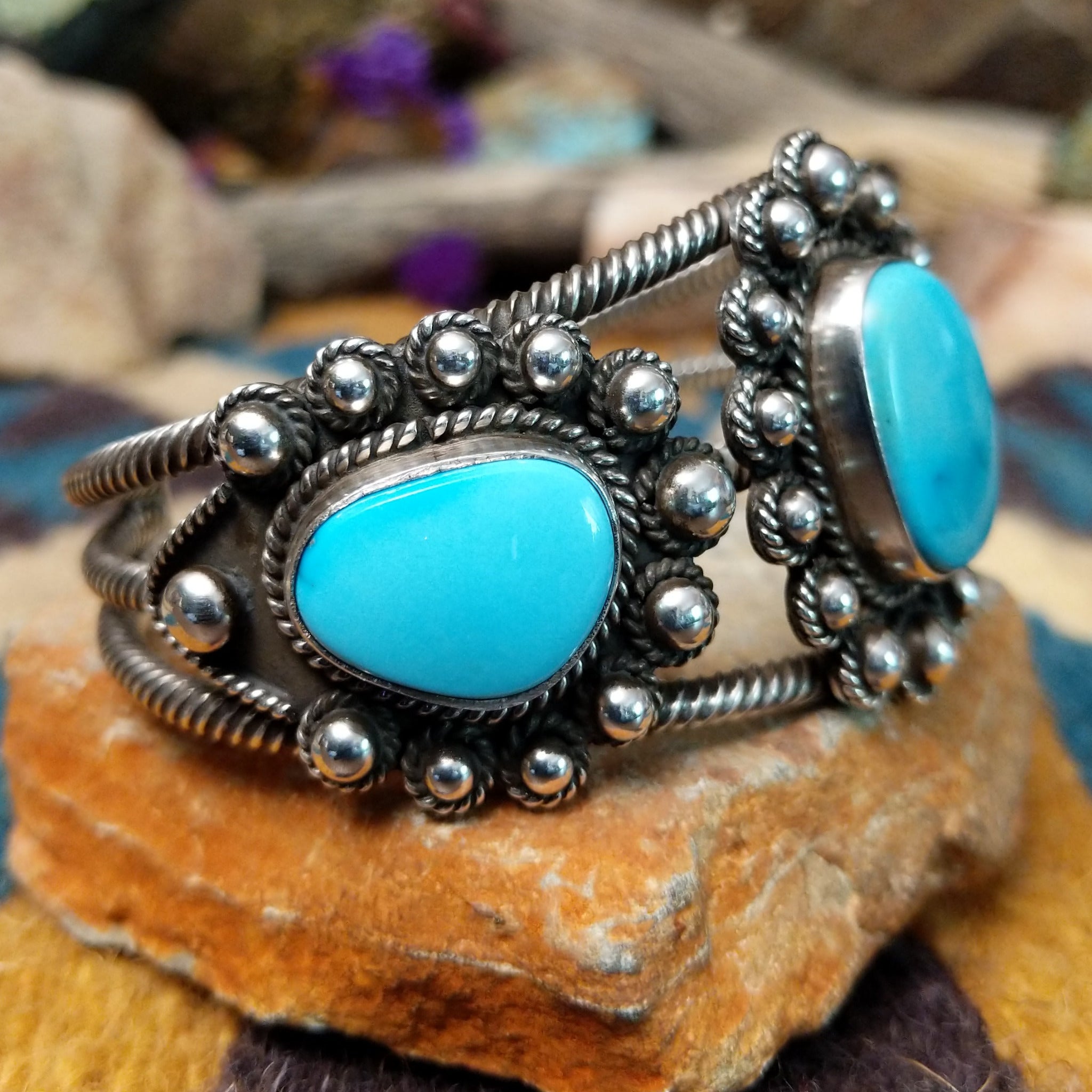 Handcrafted sterling silver cuff by Linda Johnson featuring three vibrant turquoise cabochons with twisted rope bezels, ornate silver beadwork, and a classic double-wire cuff design; side view.