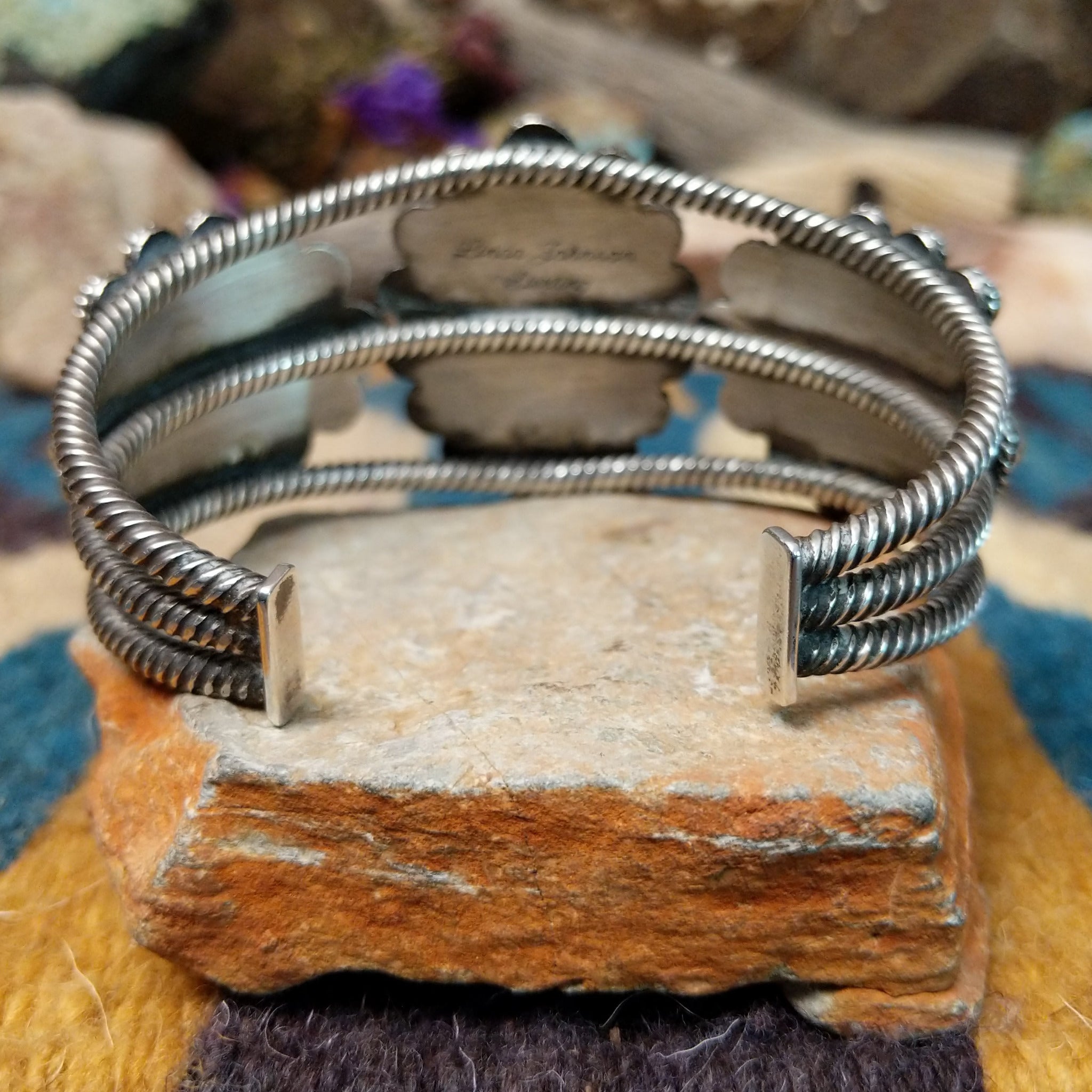 Handcrafted sterling silver cuff by Linda Johnson featuring three vibrant turquoise cabochons with twisted rope bezels, ornate silver beadwork, and a classic double-wire cuff design; underside view.