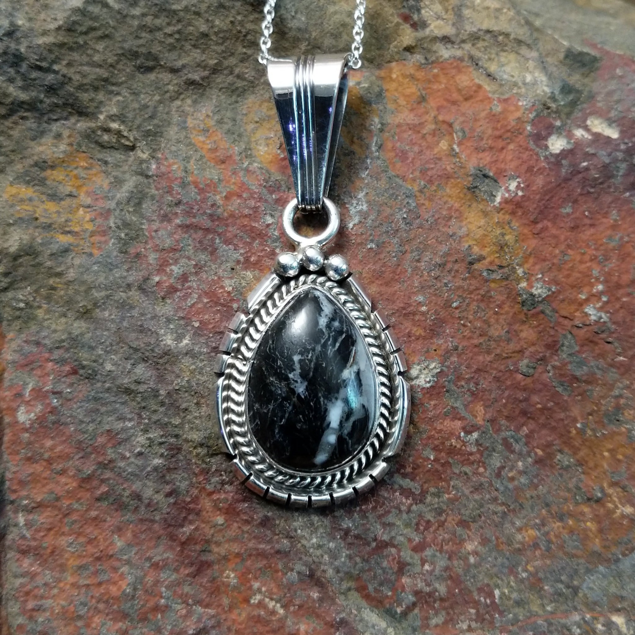 Handcrafted sterling silver White Buffalo teardrop pendant by Samuel Yellowhair, featuring a natural black-and-white White Buffalo gemstone in a twisted rope bezel.