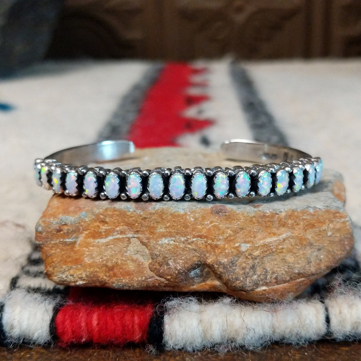 Silver cuff by Raymond Coriz featuring a single row of oval white manmade opals with colorful flashes of pink, green, yellow, and blue.