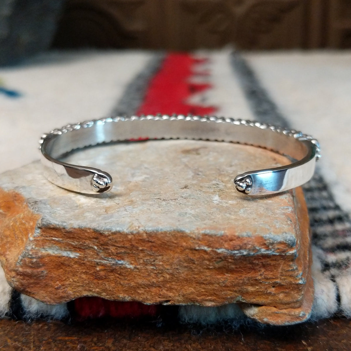 Silver cuff by Raymond Coriz featuring a single row of oval white manmade opals with colorful flashes of pink, green, yellow, and blue; underside view.